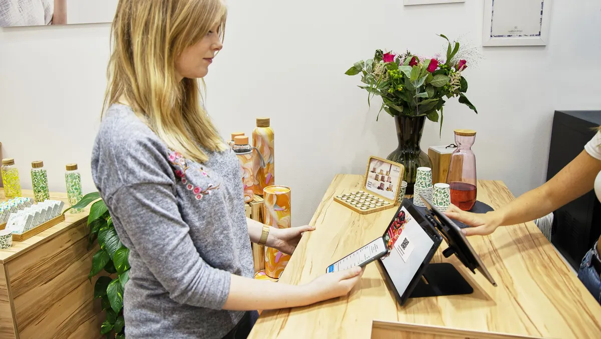 Frau steht an einem Ladentresen mit Blumen und Flaschen und tippt auf ein Tablet