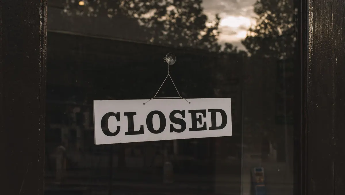 Schild „Closed“ hängt hinter der Glastür eines Ladens, dahinter Bäume und Abendhimmel